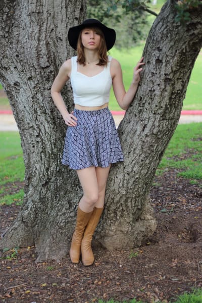 Lifestyle portrait in a patterned skirt and wide-brim hat framed by a split tree