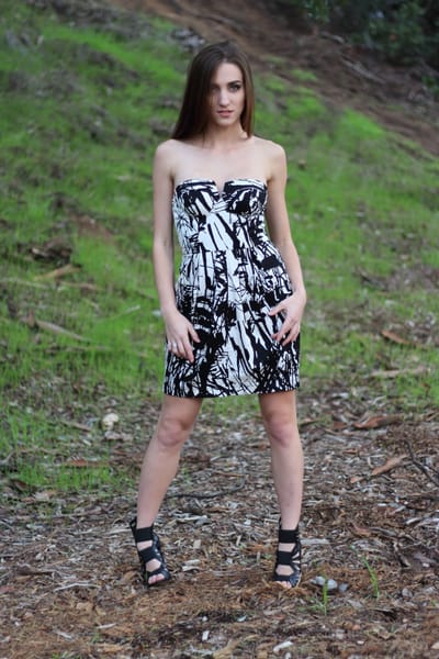 Full-length portrait in a black-and-white patterned dress on a grassy slope